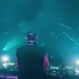 DJ plays live set under teal lasers at 0:01