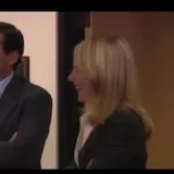 Suited coworkers chat in an office scene at 0:01