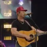 Singer in red cap performs live on stage at 0:27