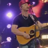 Singer in red cap performs live on stage at 0:13