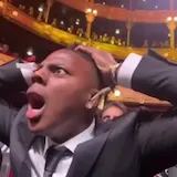 Man in suit reacts with shock in theater audience at 0:09