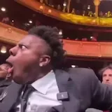 Man in suit reacts with shock in theater audience at 0:01