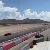 Red sports car laps desert racetrack at 0:05