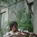 María Dueñas plays Chant de la Veslemøy on violin in a green courtyard at 0:01