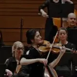 María Dueñas plays Chant de la Veslemøy on violin in a green courtyard at 0:23