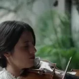 María Dueñas plays Chant de la Veslemøy on violin in a green courtyard at 0:11