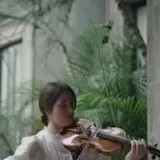 Maria Dueñas plays violin alone in a garden, then with a full orchestra at 0:11