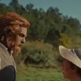 A man steps out of a hut in Wicker, greets his friends and calls at 0:07