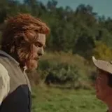 A man steps out of a hut in Wicker, greets his friends and calls at 0:14
