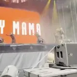 Dancers move on a lit stage as a camera peers past backstage equipment at 0:08