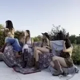 Four women lounge on rug in outdoor patio at 0:01