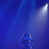 Estevie performing on blue-lit concert stage at 0:01